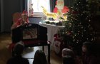 Ein Raum mit beleuchtetem Weihnachtsbaum, Rentierdeko und großem Papp-Weihnachtsmann ist zu sehen. Kinder sitzen vor einem Bildtheater. Frau Eff spielt eine Bildergeschichte mit Eichnörnchen.